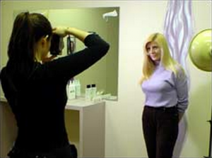 A photographer takes a picture of a woman posing in front of a mirror in a room.